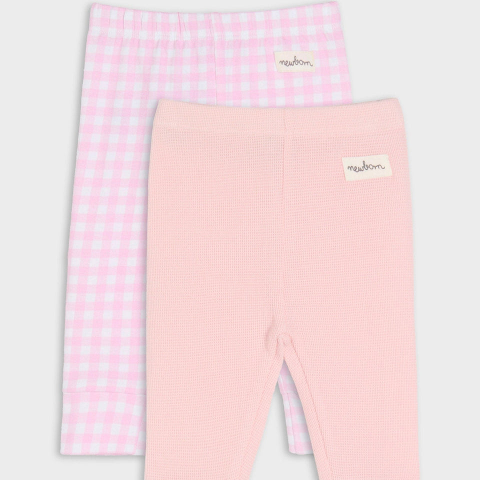 Two pairs of baby leggings from the brand 'meadon' shown on a light gray background. The front pair is light pink with a fine ribbed texture, and the back pair is light pink and white gingham check.