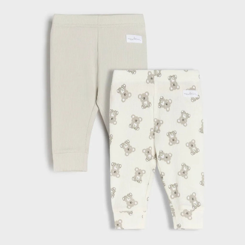 Two pairs of baby leggings laid flat on a light gray background. The back pair is solid cream, and the front pair is cream with a repeating teddy bear print in beige and brown.