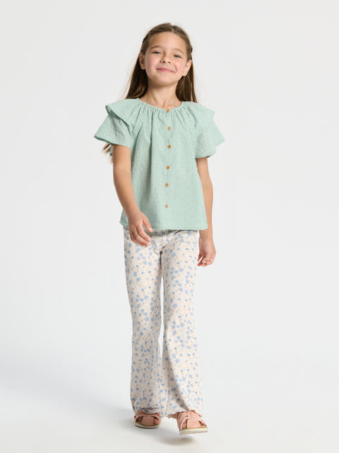 Young girl wearing a light green blouse and floral pants on a white background