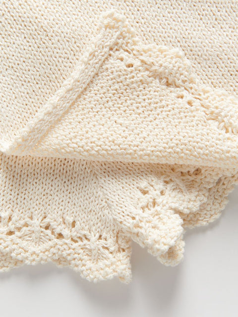 Close-up of a cream-colored knitted fabric with lace detailing on a white background