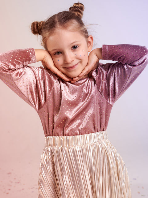 Young girl wearing a sparkly pink top and beige skirt against a light background