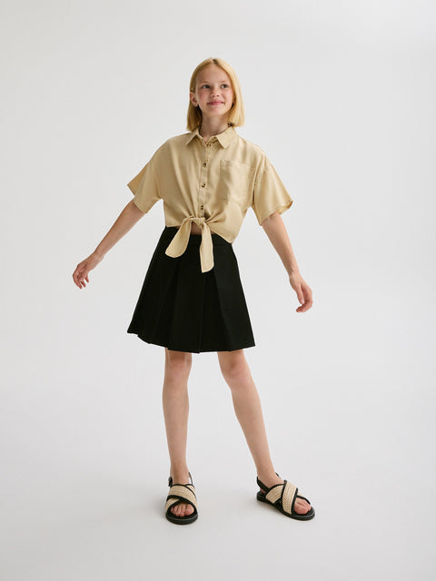 Young girl wearing a beige shirt and black skirt on a white background