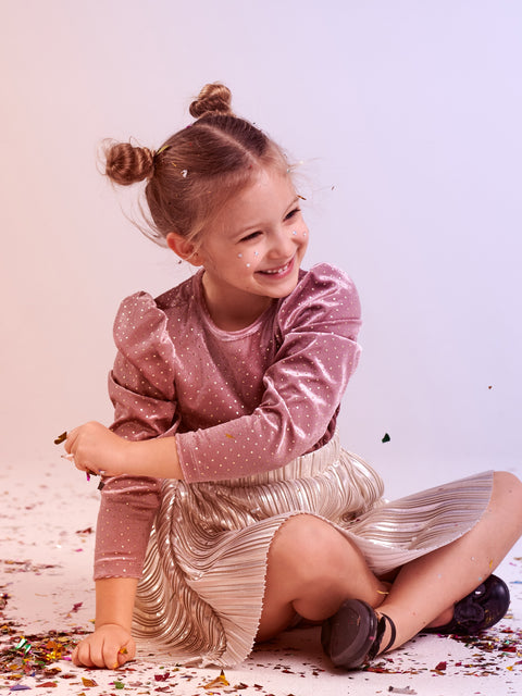 Young girl in a pink top and silver skirt sitting on the ground with a white background