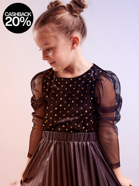 Young girl wearing a black dress with sheer sleeves on a light pink background
