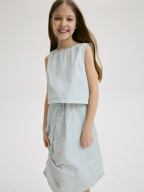 Young girl wearing a light blue sleeveless top and cargo shorts on a white background