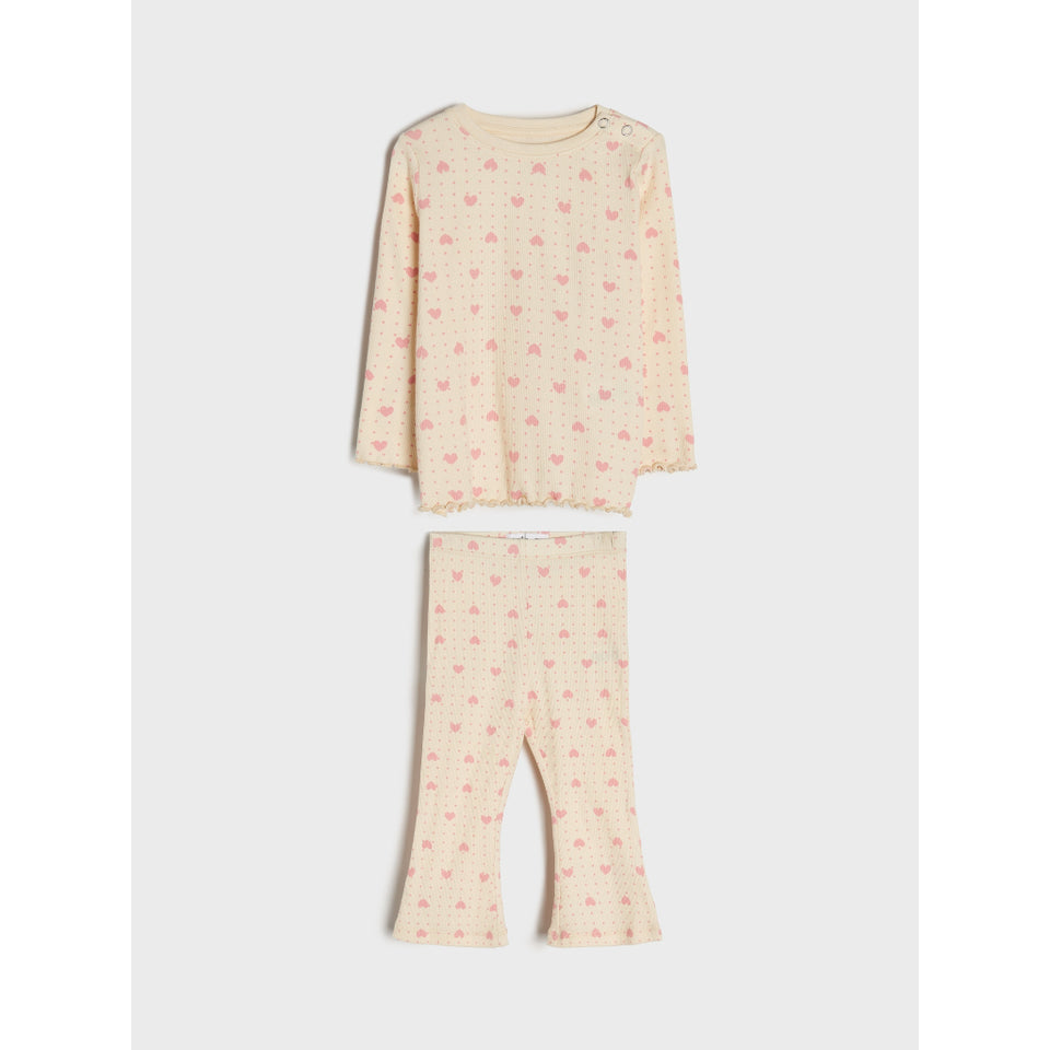 A two-piece children's pajama set featuring a long-sleeve top and matching flared pants in a light cream color with a small pink heart pattern, laid flat against a light gray background.
