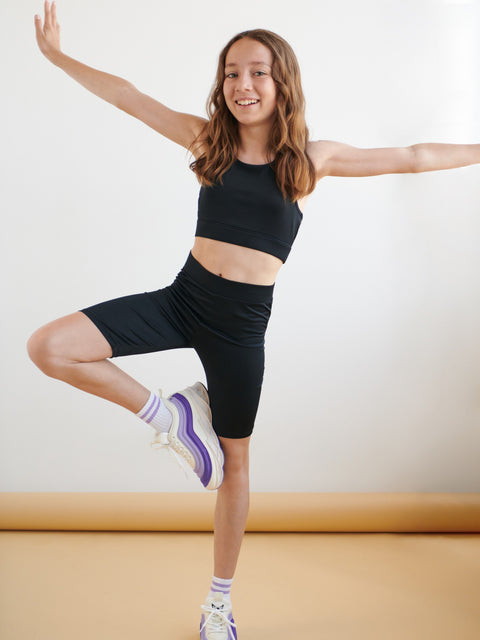 Woman in black athletic wear posing with one leg raised on a light background
