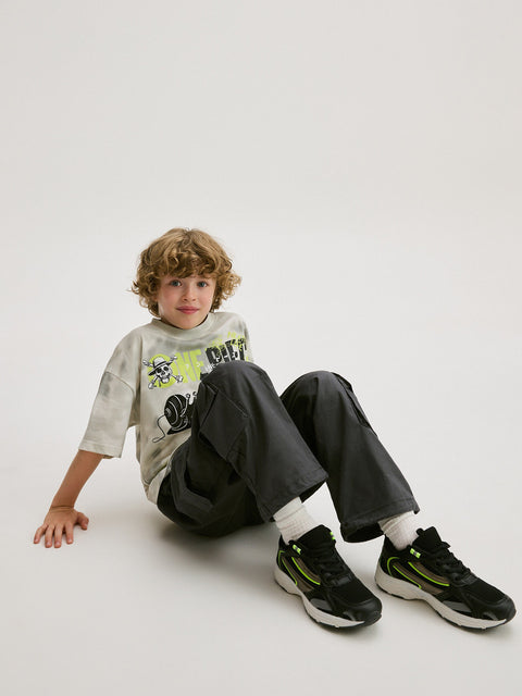 Child sitting on the floor wearing a graphic t-shirt, dark pants, and black shoes.