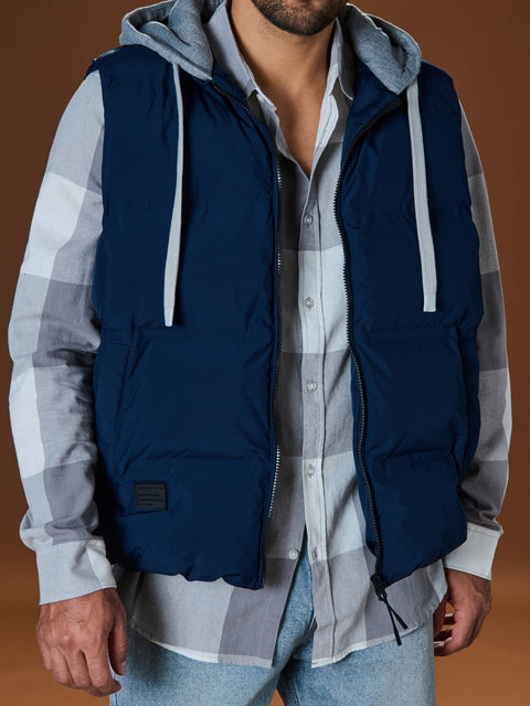 Person wearing a navy puffer vest over a plaid shirt on a brown background