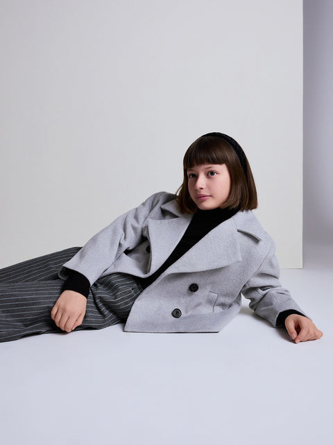 Person wearing a gray coat sitting on a white floor against a light gray wall.