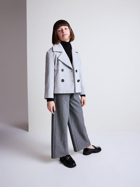 Person wearing a light gray coat, black turtleneck, and gray striped pants against a white background