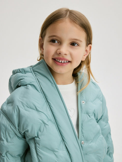 Young girl wearing a light blue puffer jacket on a plain background