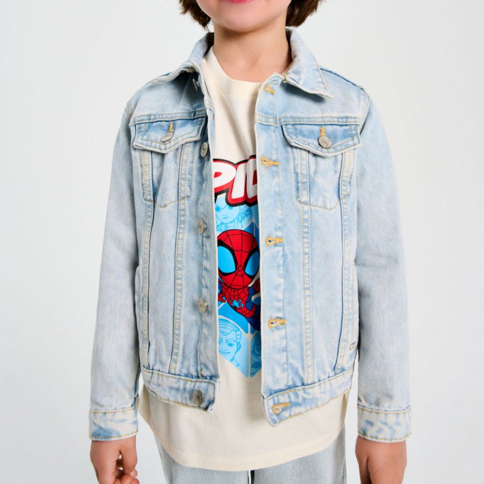A young boy with brown hair wearing a light wash blue denim jacket over a cream graphic t-shirt featuring Spider-Man, standing against a plain light gray background.