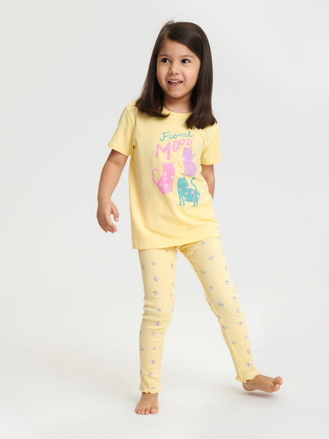 Young girl wearing a yellow pajama set with cartoon characters on a white background