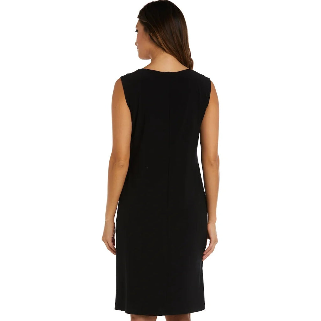 A woman viewed from the back wearing a sleeveless black knee-length dress and tan high heels against a plain white background.