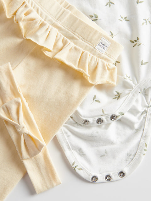Close-up of a baby outfit with ruffled top and white pants on a light background