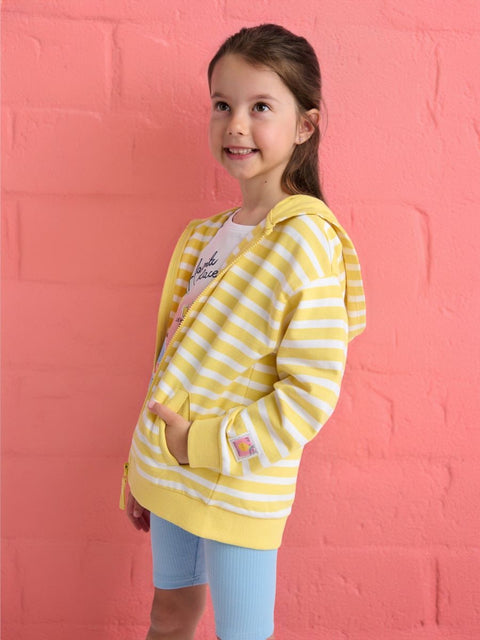 Young girl wearing a yellow striped hoodie against a pink wall