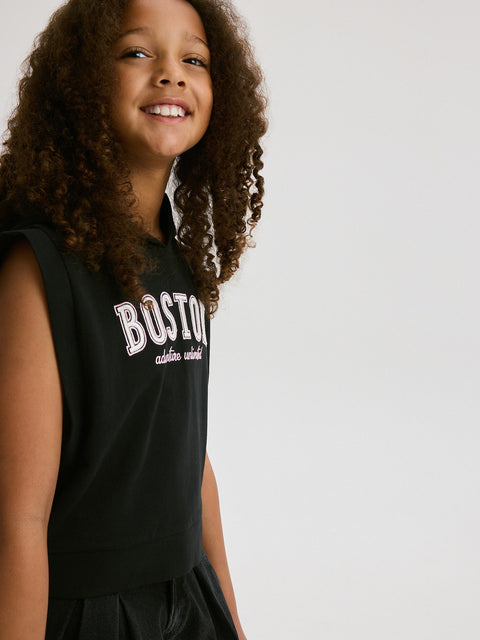 Young girl wearing a black sleeveless shirt with 'Boston' printed on it against a plain background