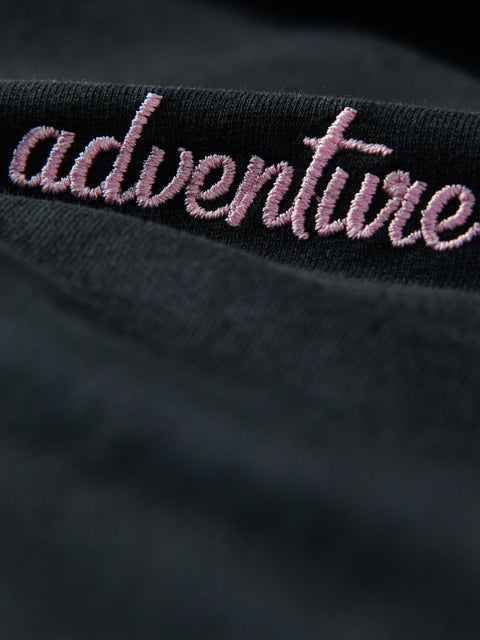 Black fabric with pink embroidered text 'adventure' on a dark background