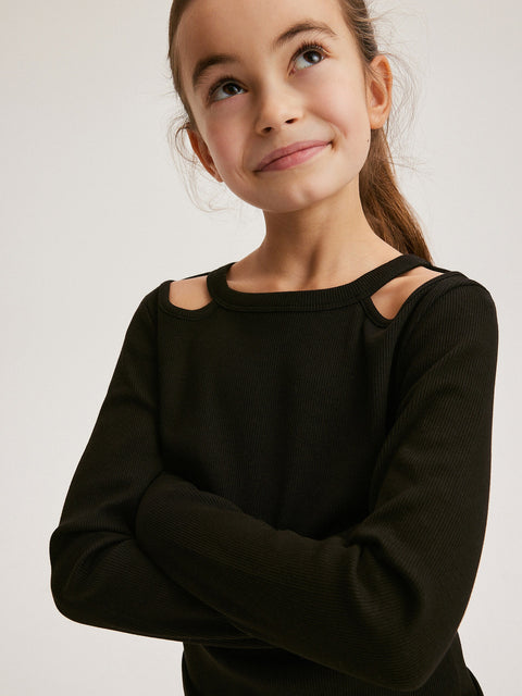 Young girl wearing a black long-sleeve top with cut-out shoulders on a light gray background