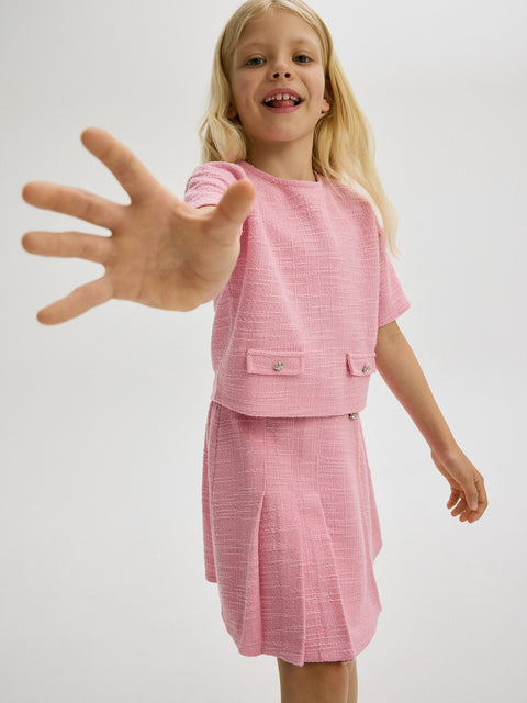Young girl in a pink outfit reaching out with her hand against a white background