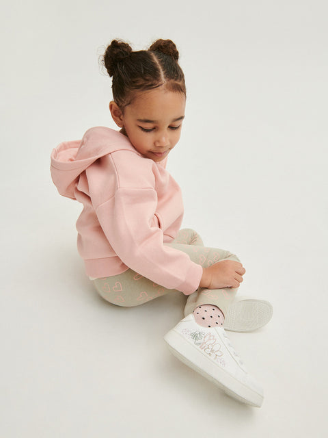 Child wearing a pink hoodie and white shoes on a light background