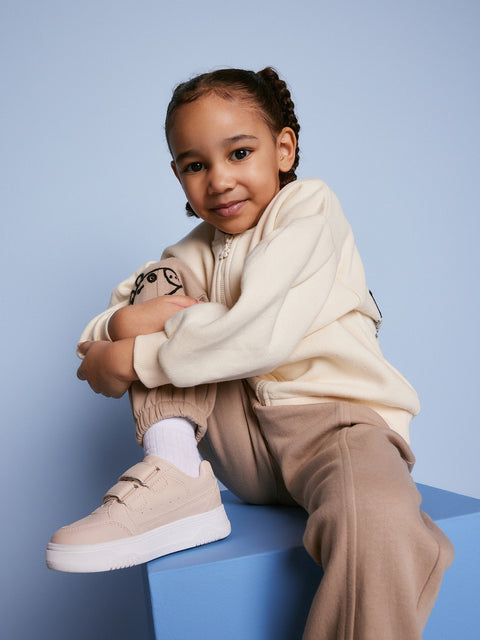 Child wearing a beige outfit with white sneakers on a blue background