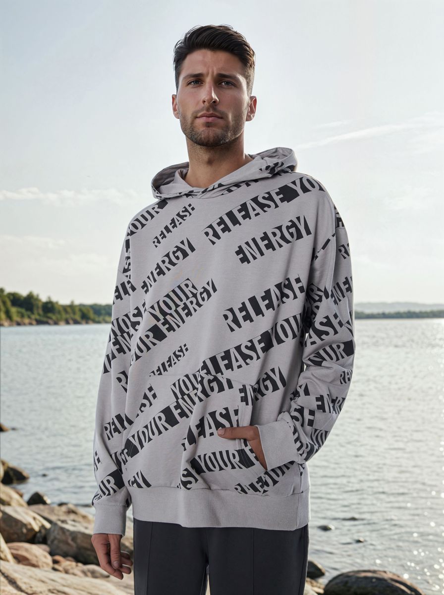 Man wearing a gray hoodie with black text pattern by a body of water
