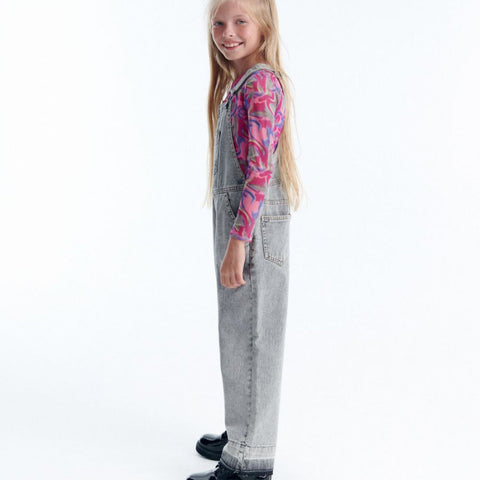 Young girl wearing gray overalls with a colorful shirt on a white background