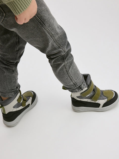 Child wearing black and green high-top sneakers on a white background