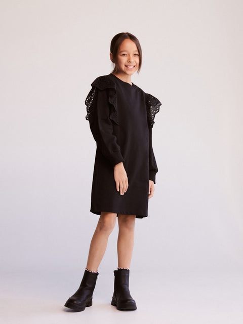 Young girl wearing a black dress with ruffled shoulders on a white background
