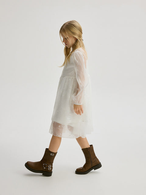 Person wearing a white dress and brown boots on a plain background