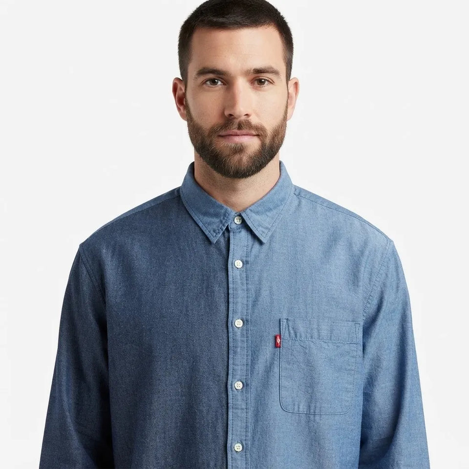 A man wearing a medium blue chambray button-down shirt with a chest pocket and a small red Levi's tab, photographed against a clean white background.