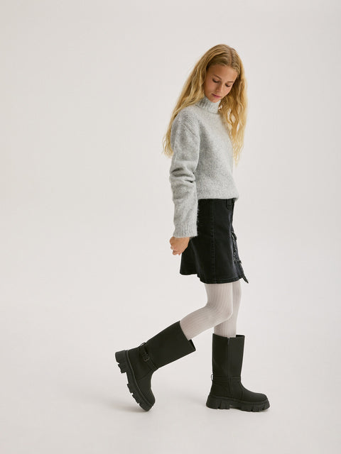 Person wearing a gray sweater, black skirt, and black boots on a white background