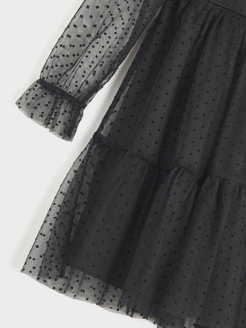 Black polka dot dress with sheer overlay on a white background
