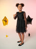 Young girl in a black dress standing between two balloons against a light pink background
