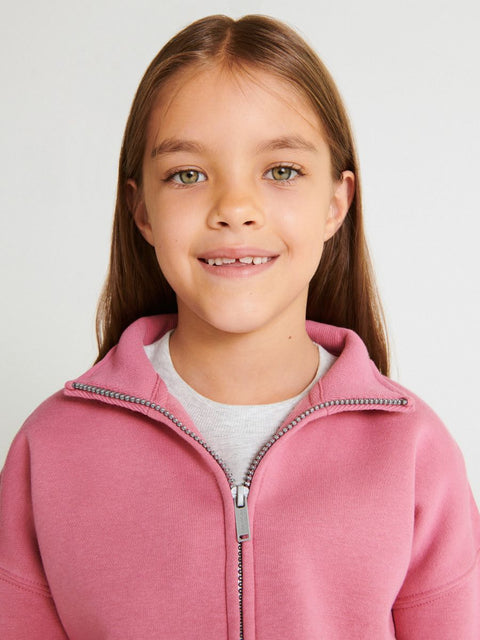 Young girl wearing a pink zip-up hoodie against a plain background