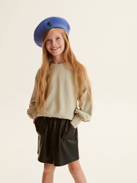 Young girl wearing a blue beret and beige sweater with a black skirt on a light background