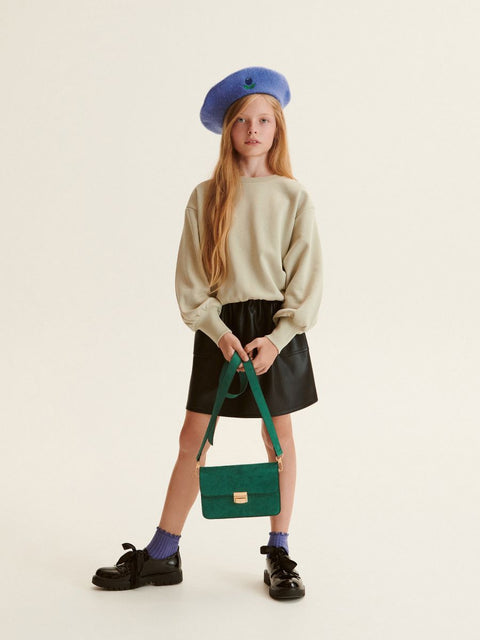 Young girl holding a green handbag against a plain background