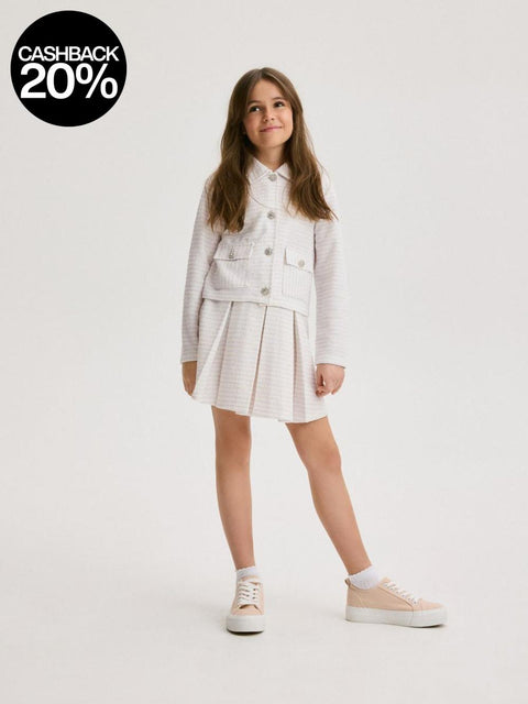 Young girl wearing a white outfit with a jacket and skirt on a light gray background