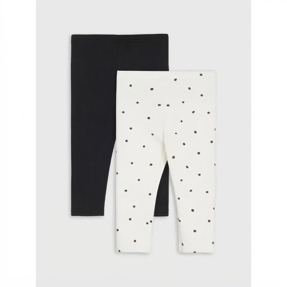 Two pairs of children's leggings displayed flat against a light gray background. The pair on the left is solid black, and the pair on the right is off-white with a scattered small dark polka dot pattern.