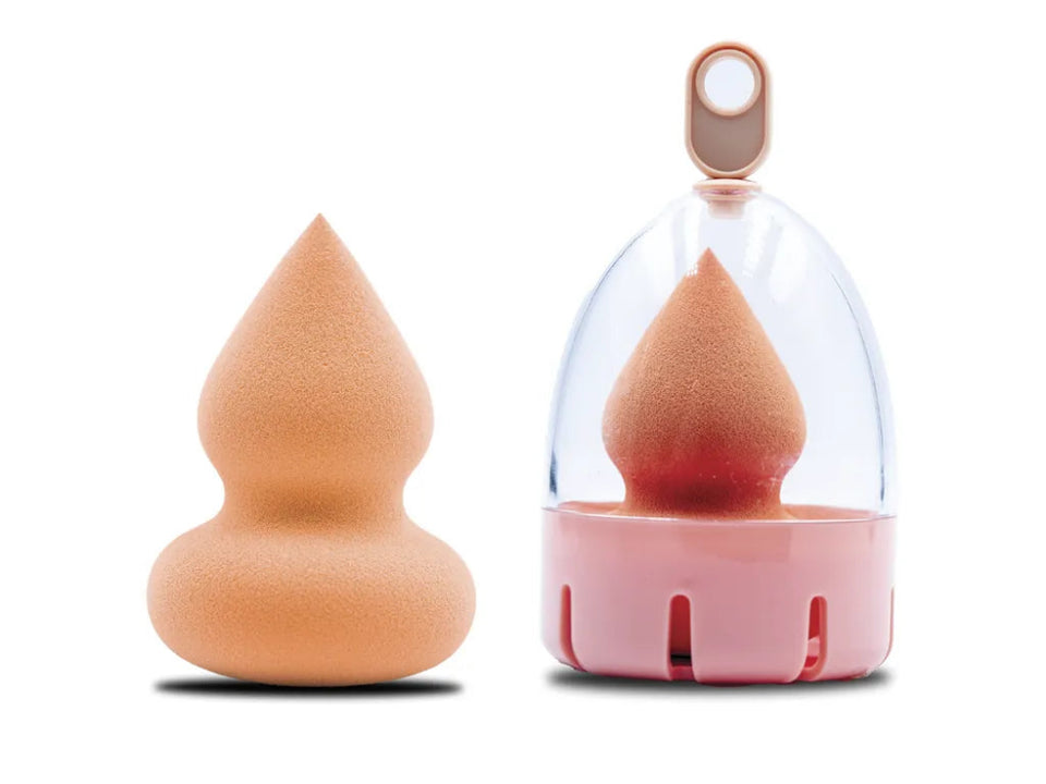 A beige-colored beauty blender sponge with a pointed tip, displayed alongside its pink and clear holder.
