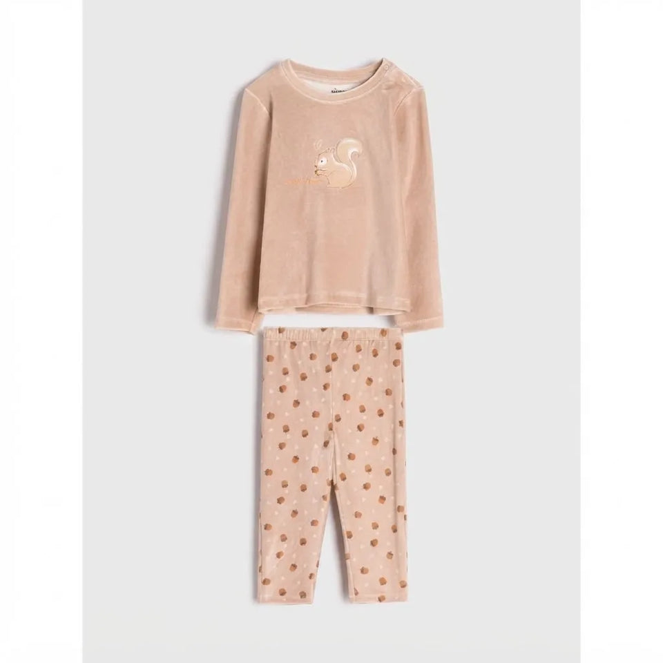A two-piece children's pajama set in a soft peach-beige velour fabric, featuring a long-sleeve top with a small embroidered squirrel on the chest and matching patterned pants.
