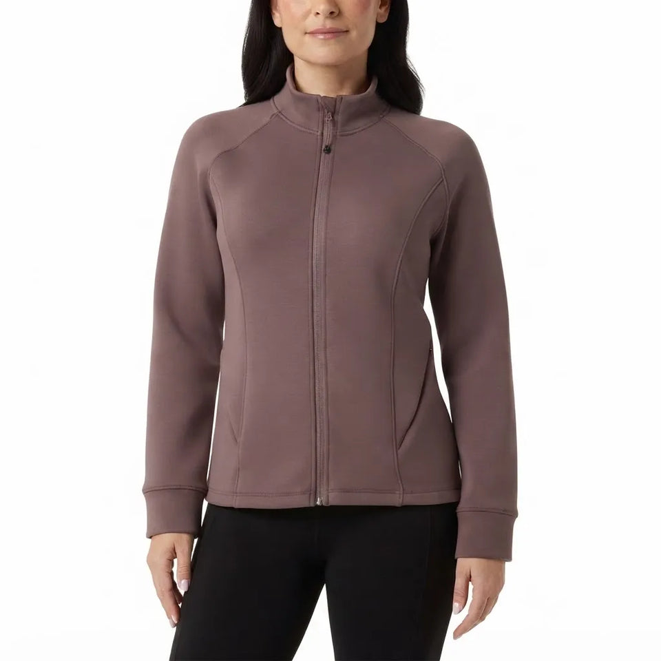 A woman wearing a fitted zip-front jacket in a muted taupe-brown color, paired with black pants, against a plain white studio background.