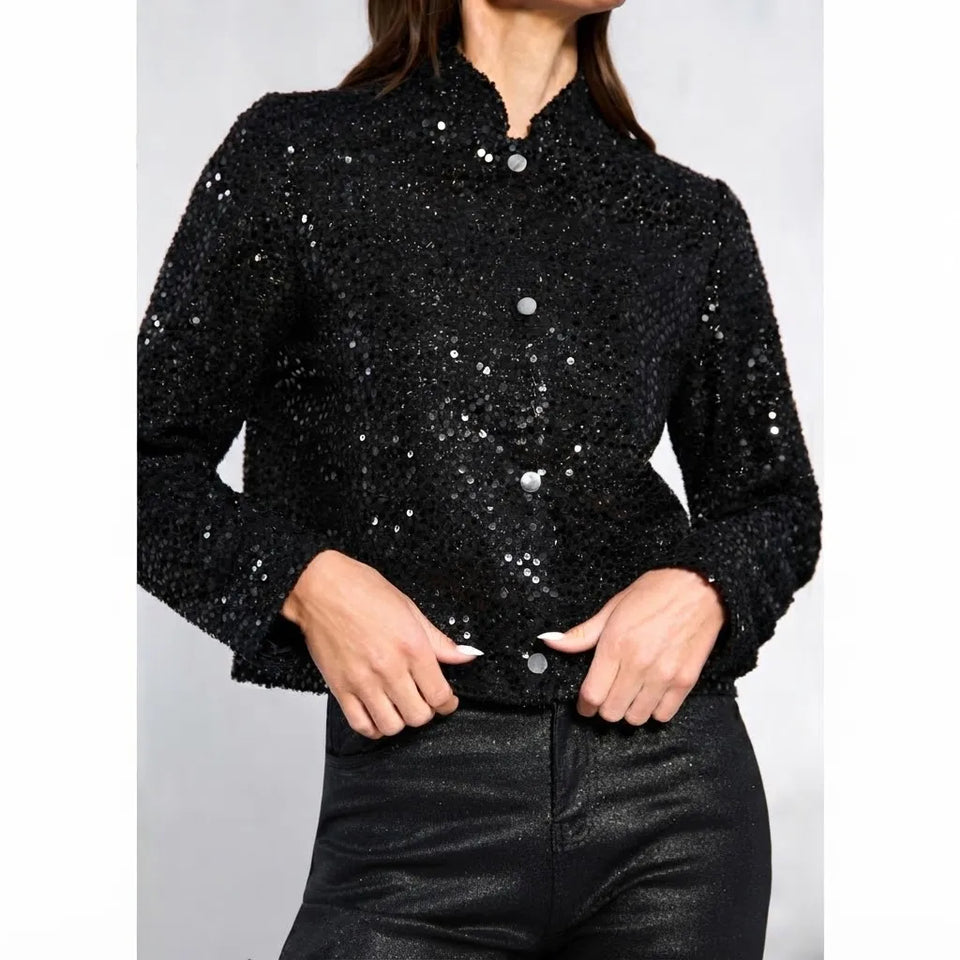 A woman wearing a black sequined jacket with a stand-up collar and front buttons, paired with black pants, shown against a plain light gray background.