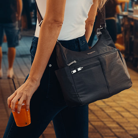 Person holding a black bag and an orange drink on a street.