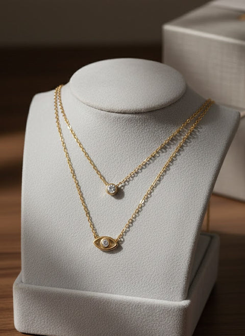 Two gold necklaces on a white jewelry stand with a blurred background