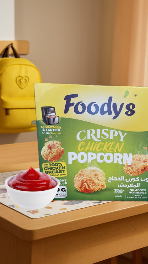 Foody's Crispy Chicken Popcorn packaging on a table with a yellow backpack in the background