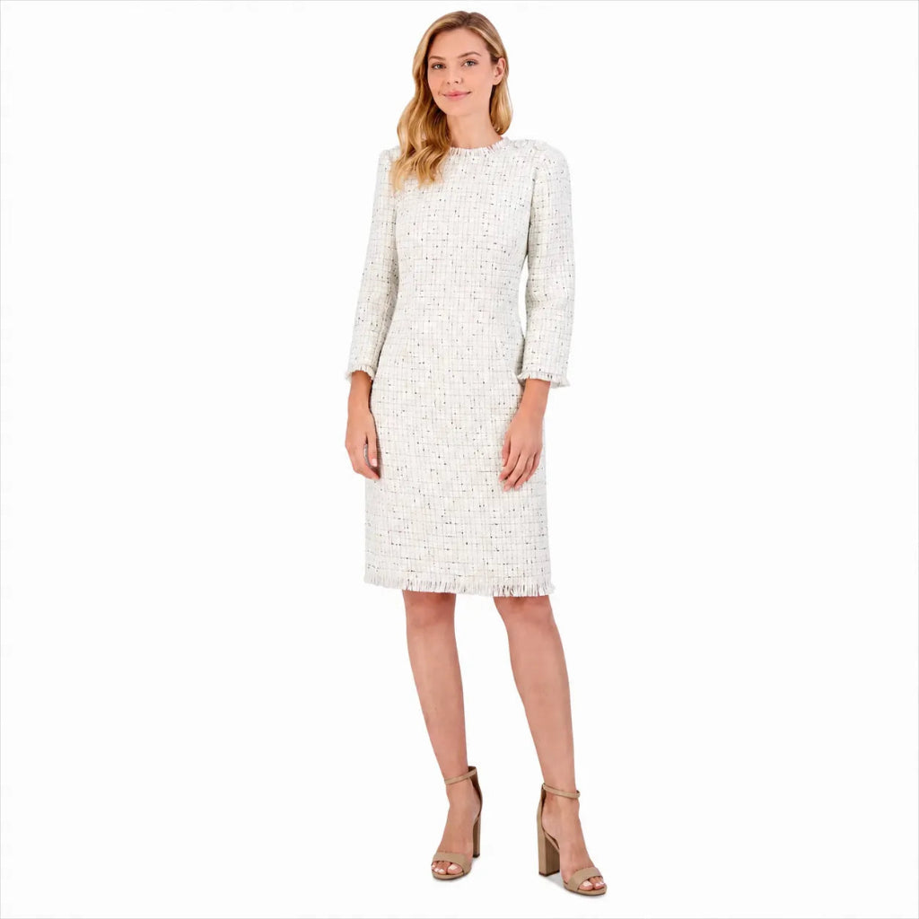 A woman modeling a white and beige tweed knee-length dress with three-quarter sleeves and fringed edges, paired with beige high-heeled sandals, against a plain white background.