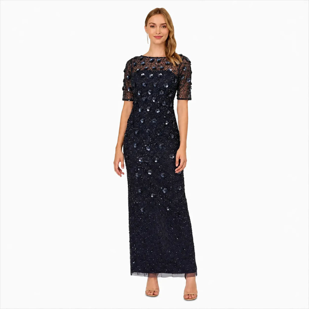 A woman modeling a floor-length navy blue gown with short sheer lace sleeves and scattered silver sequins, photographed against a plain white background.